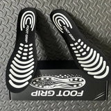 Photo client : paire de semelles Foot Grip noires posées sur leur boîte, sur un tapis gris